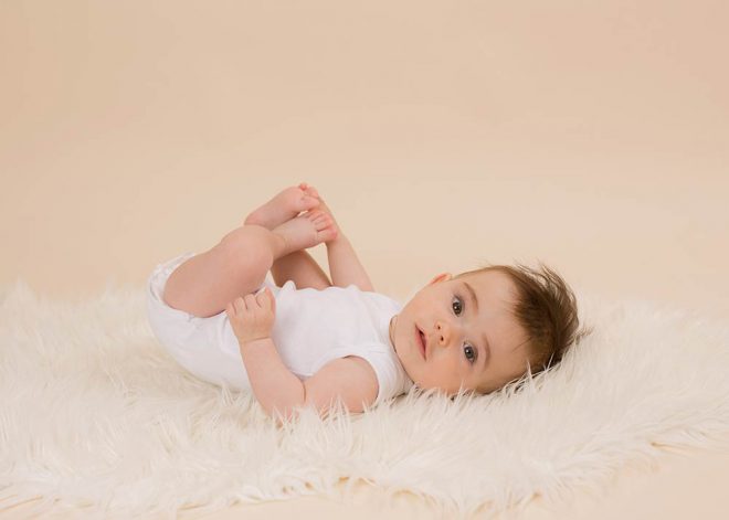 Babyfotos Berlin: Baby mit dunklen Haaren liegt mit dem Rücken auf einem weißen Fell