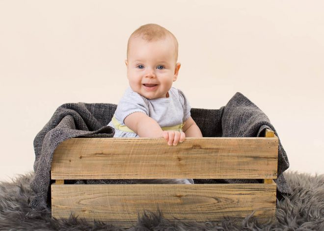 Babyfotos Berlin: Kleines Mädchen sitzt in einer Holzkiste und lacht