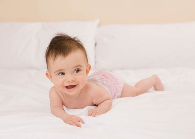 Babyfotos Berlin: Mädchen in rosa Hose liegt auf einem Bett und lacht