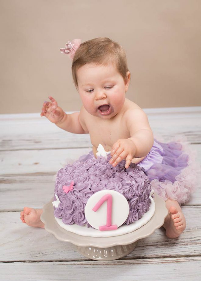 Kleines Mädchen feiert ersten Geburtstag mit einer lila Torte