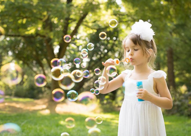 Kinderfotos Berlin: Mädchen in weißem Kleid pustet bunte Seifenblasen