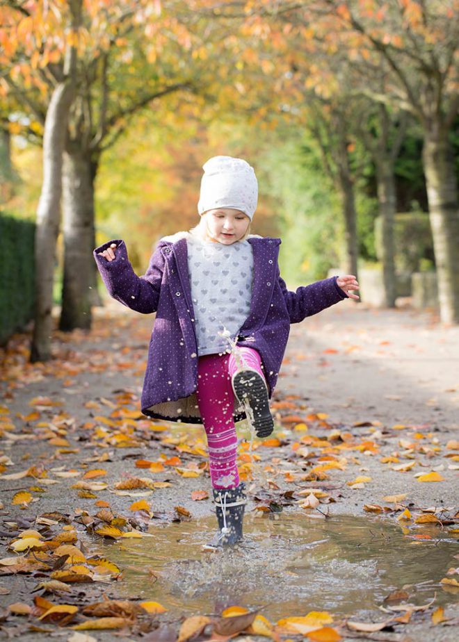 Mädchen spielt im Herbst in einer Regenpfütze mit Gummistiefeln