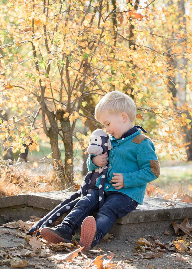 Junge mit blonden Haaren und Stofftier vor Herbstlaub