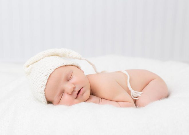 Neugeborenenfotos Berlin: Neugeborenes mit weißer Strickmütze in Bauchlage