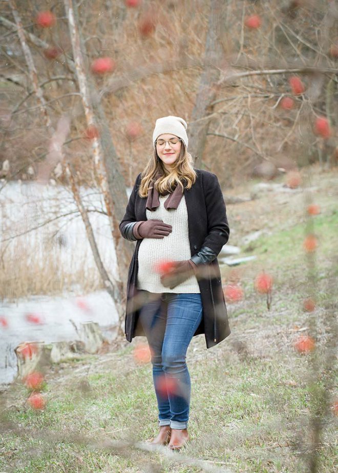 Babybauchfotos Berlin: Schwangere Frau mit Mütze und Handschuhen steht auf einer Winterwiese