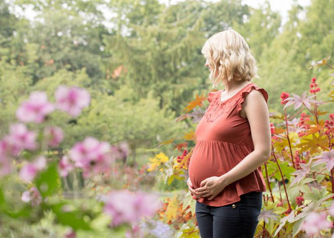 Schwangere steht im Sommer zwischen Blumen