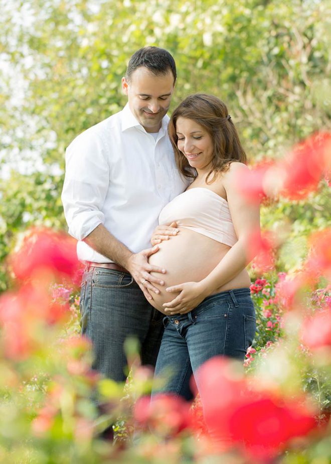 Paar schaut auf ihren Babybauch und ist von Rosen umgeben