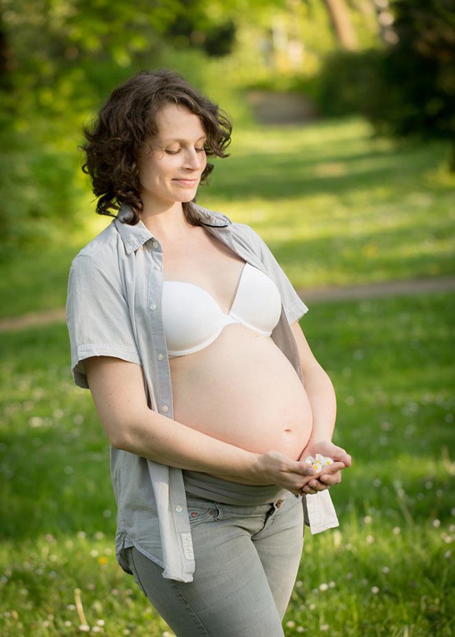 Schwangere im Sommer hält sich Gänseblümchen an den Bauch