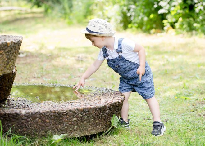 Kinderfotos Berlin: Junge mit Hut spielt an einem Brunnen