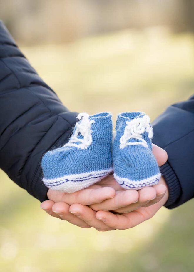 Zwei Hände halten blaue Babyschuhe