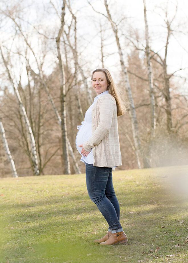 Schwangere Frau steht vor kleinem Birkenwald im Winter