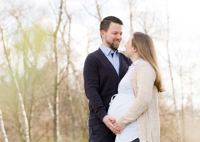 Babybauch Shooting im Winter: Schwangeres Pärchen lächelt sich an