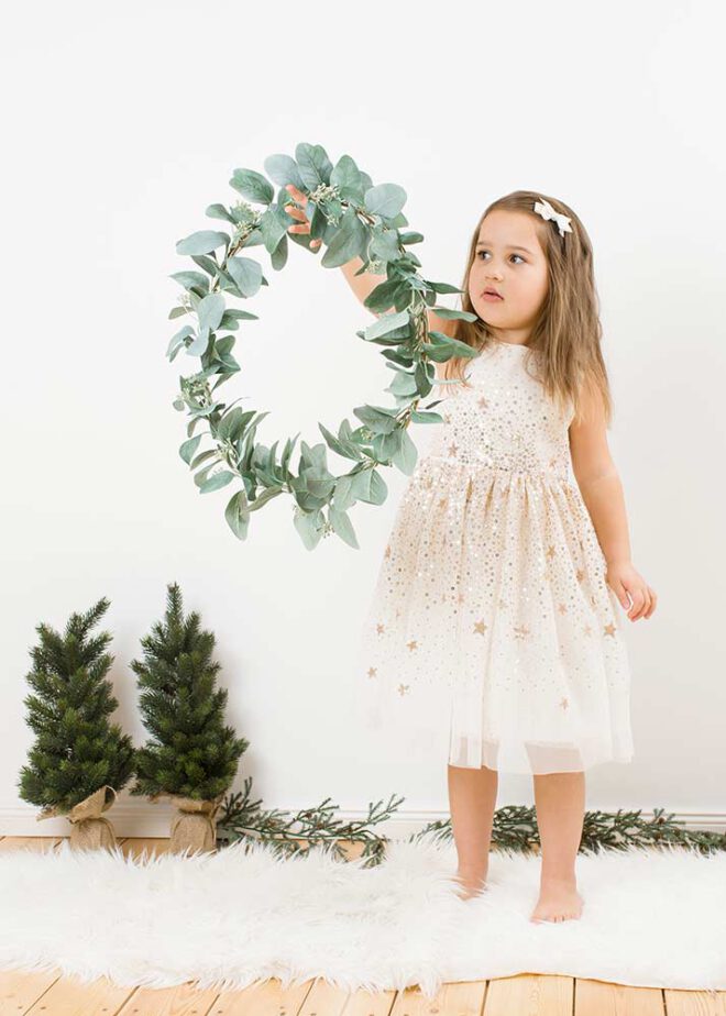 Mädchen hält bei minimalistische Weihnachtsfotos einen Kranz