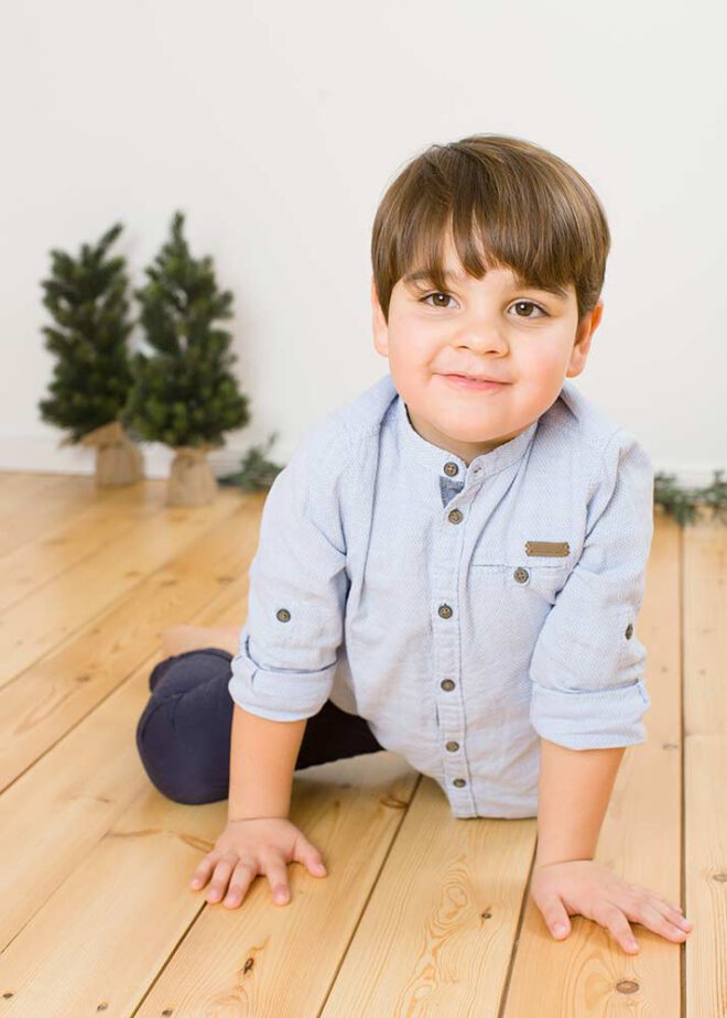 Kleiner Junge in blauem Hemd sitzt auf dem Boden und lächelt in die Kamera